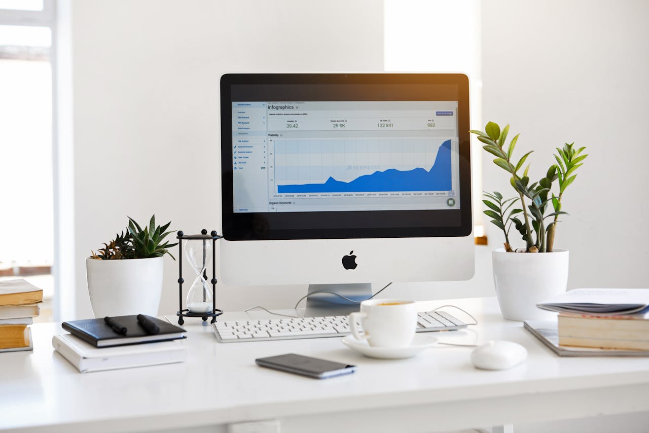 heros-img A clean, contemporary workspace featuring a desktop with analytics on the screen and plants for a fresh look.